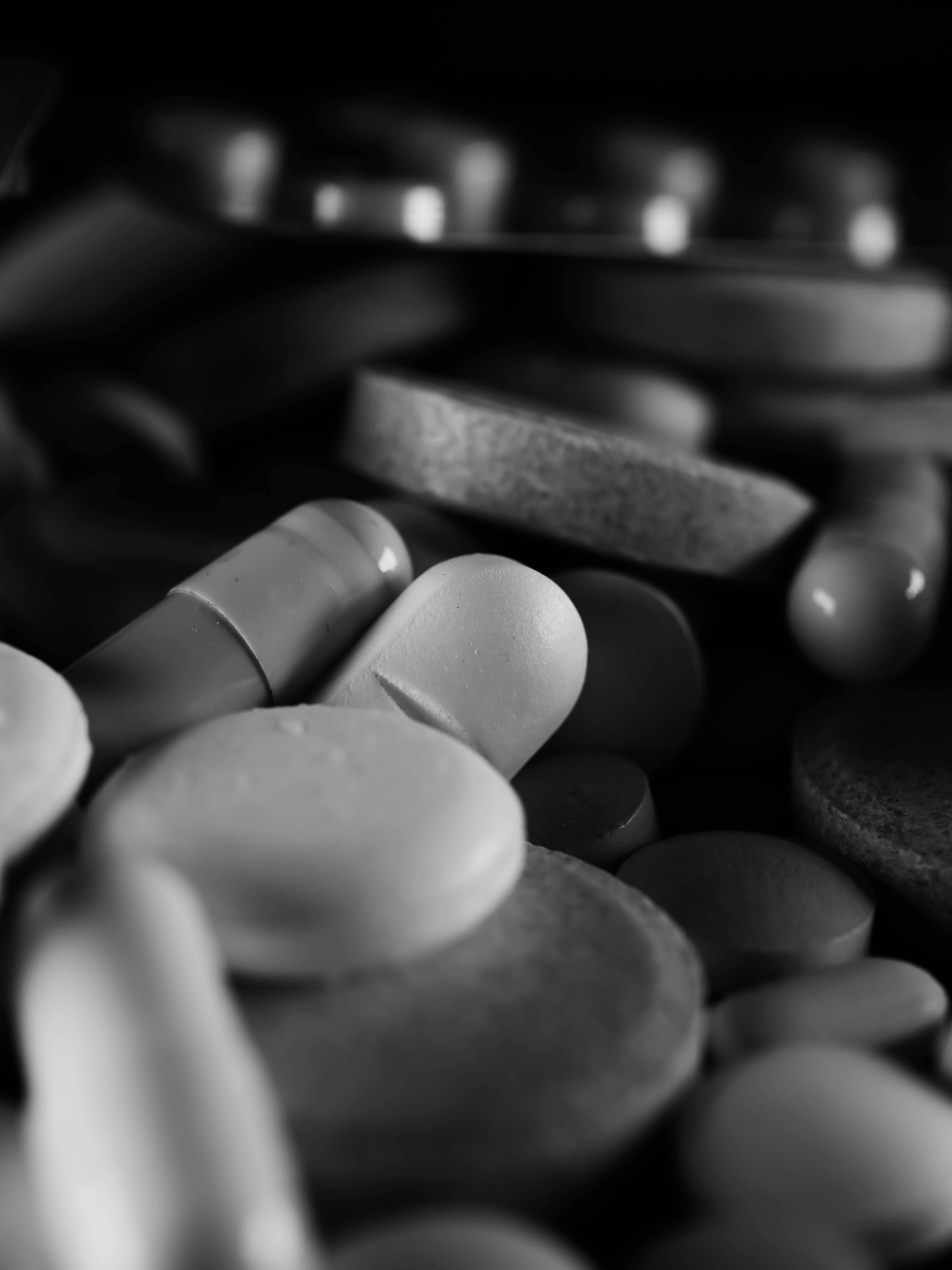 Black and white macro shot of assorted pills and capsules, highlighting textures.